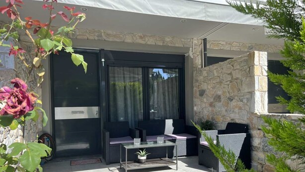 An outdoor patio with a glass door, stone walls, and a seating area with a table and chairs. - Vero Resort Townhouse Hanioti (Халкидики)