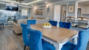 A modern kitchen with a dining area, featuring a wooden table, blue upholstered chairs, and a chandelier.
