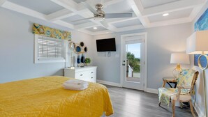 A bedroom with a large bed, a ceiling fan, a TV, a dresser, and a chair.