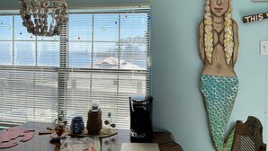 A room with a large mermaid sculpture, a coffee maker, and a window with blinds.