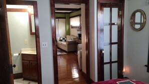 A room with a wooden floor, a bed with a red blanket, a bedside table, and a mirror on the wall. - 1800s Home, Train-Themed Decor, Walk to Downtown & Attractions, Exclusive Perks (Boone)