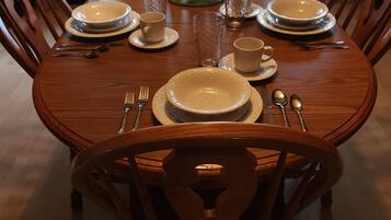 Une table à manger dressée pour six personnes, avec de l’argenterie blanche, des assiettes, des bols et des verres, entourée de chaises en bois.