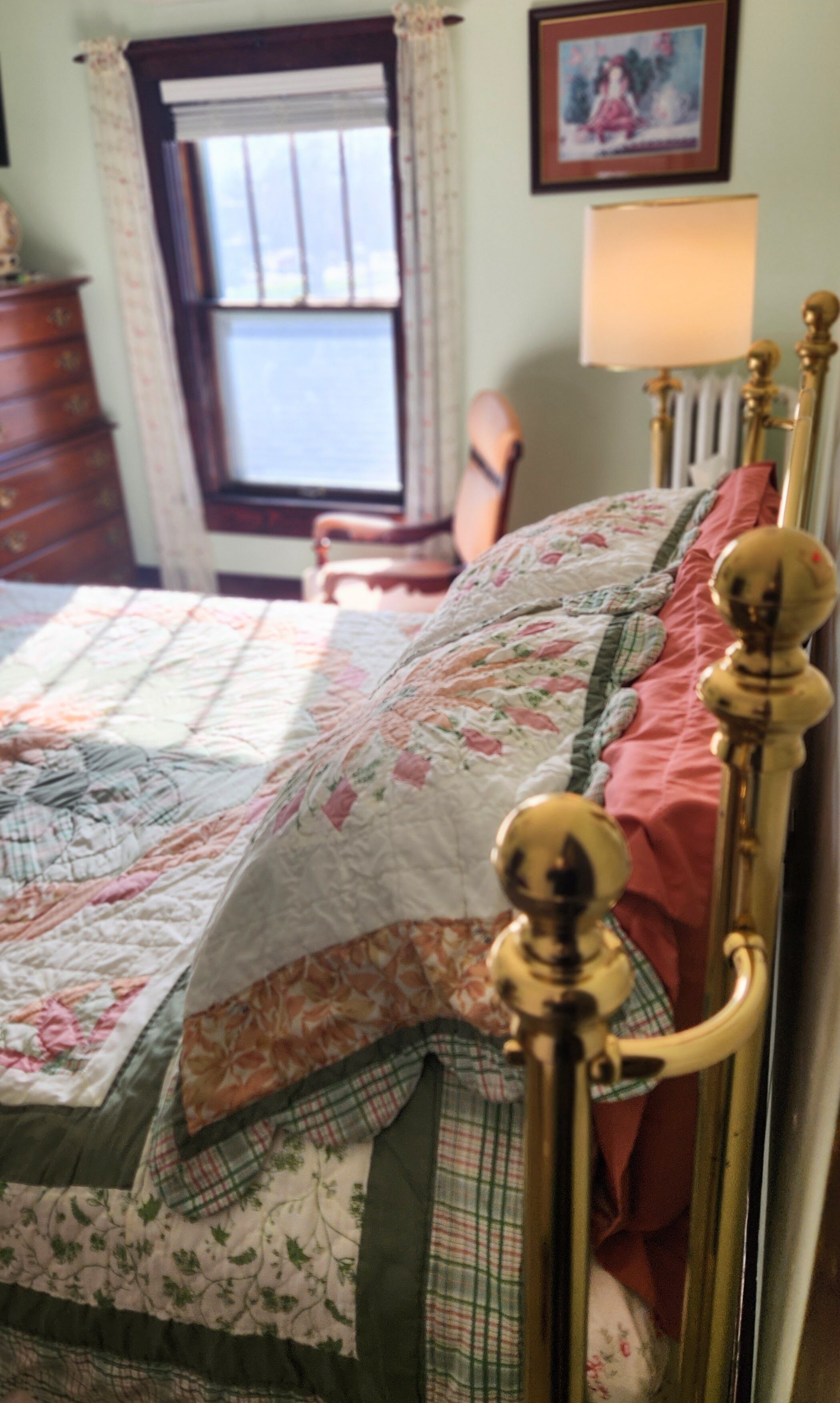 A bed with a floral quilt, a wooden headboard, and a window with curtains.