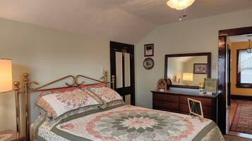Een slaapkamer met een bed, een dressoir, een spiegel en een deur naar een andere kamer.