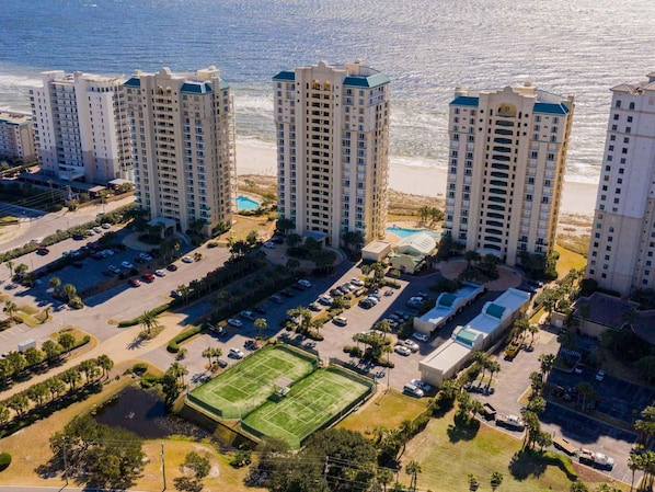 A high-rise hotel with multiple floors, a parking lot, and a tennis court. - Beach Colony West #2C | Beachfront Balcony, Luxury Finishes, & Top-Notch Ameniti (Perdido Key)