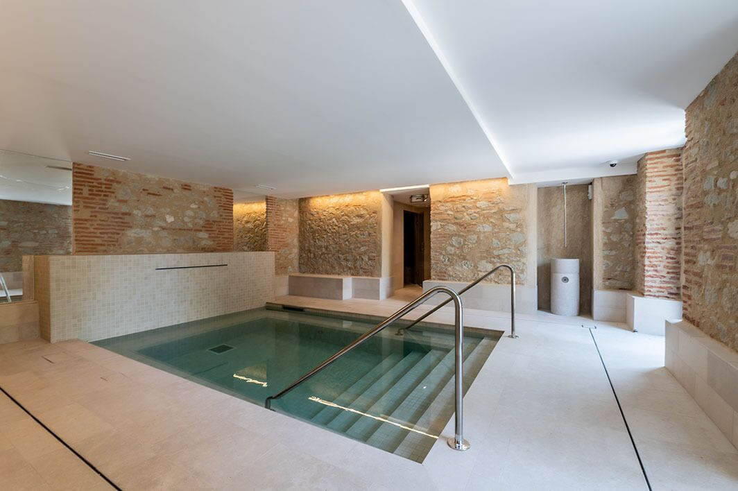 Una piscina interior moderna con paredes de piedra y una barrera de cristal.