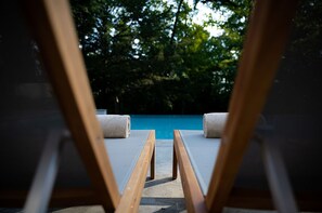 Une piscine entourée d’arbres, avec des chaises longues et des serviettes à proximité.