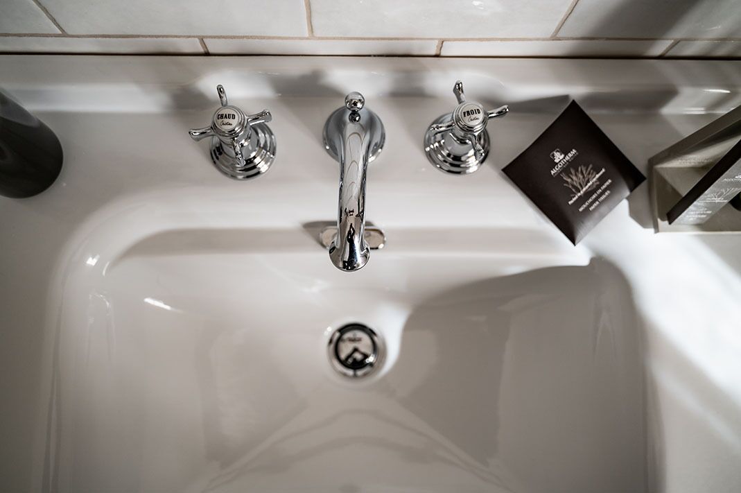 Ein weißes Waschbecken mit drei Chromarmaturen, wovon eine die Marke 'FROHD' trägt.