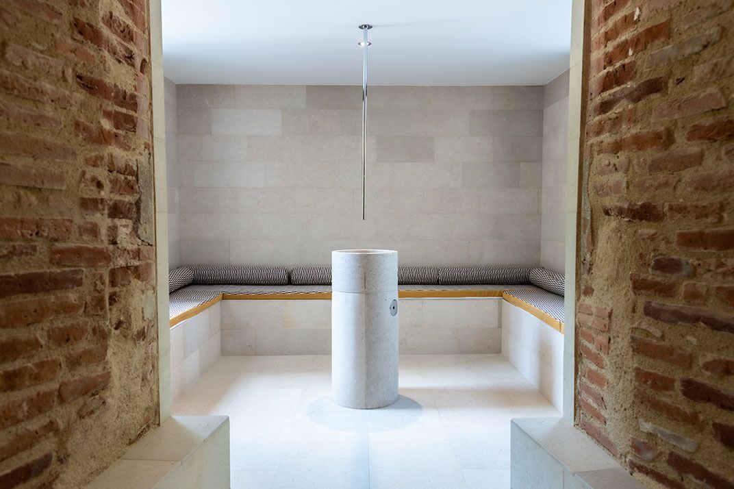A modern bathroom with a central column, a bench with cushions, and a tiled wall.