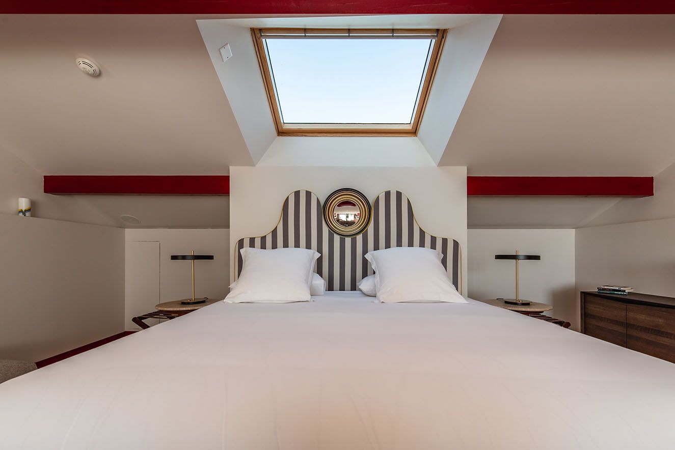 A bedroom with a skylight, a bed with white bedding, striped headboard, and bedside tables with lamps.