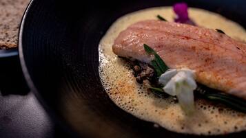 A dish with a piece of fish on a creamy sauce, garnished with herbs and a flower.