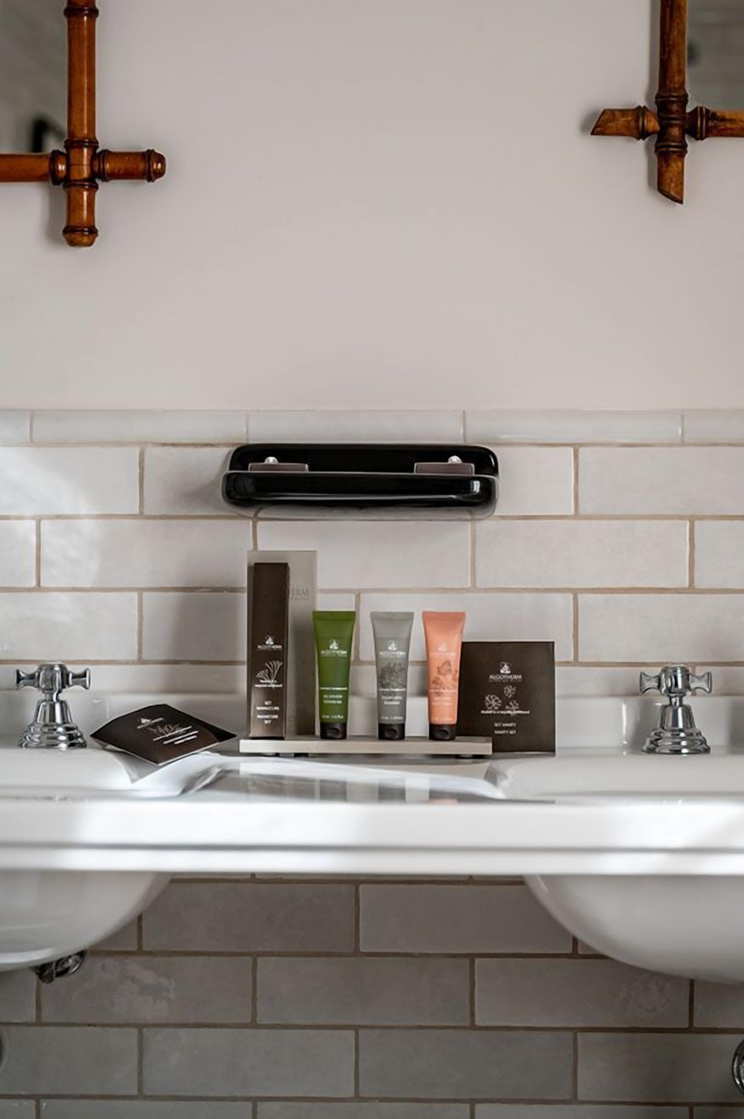 A bathroom with two sinks, a mirror, and a shelf with toiletries.