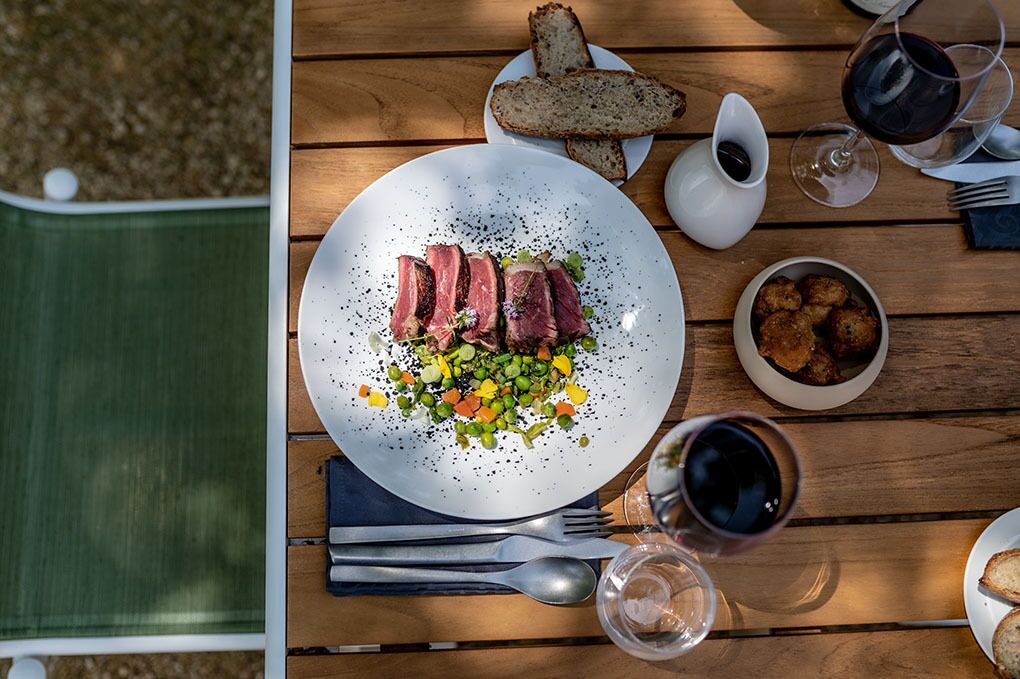 A dining table with a plate of steak, vegetables, and bread, along with wine glasses and cutlery.