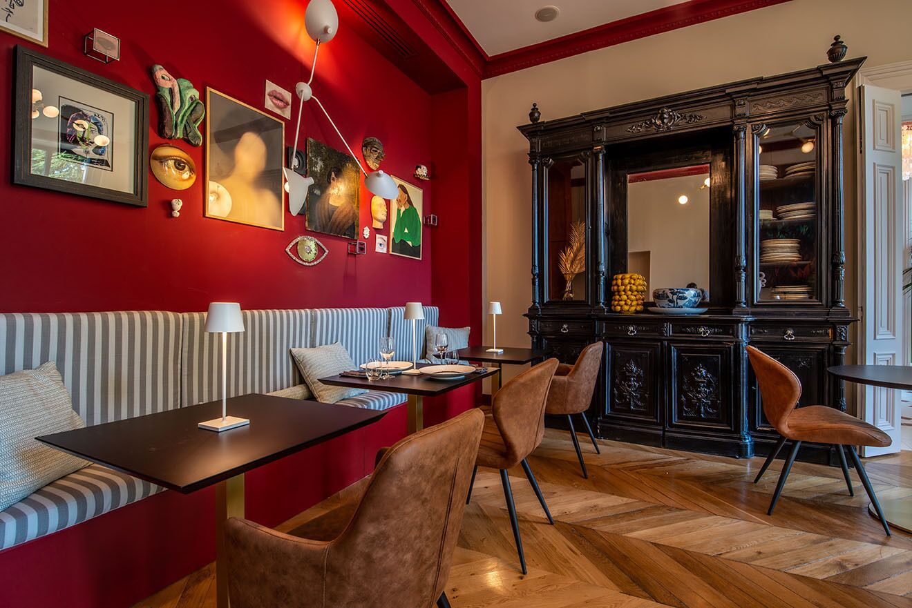 A dining area with a red wall, striped sofa, and a black cabinet with dishes.