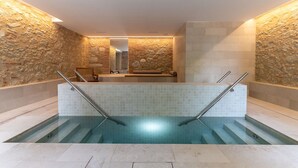 Uma área de spa com parede de pedra, piscina azulejada e um banco.