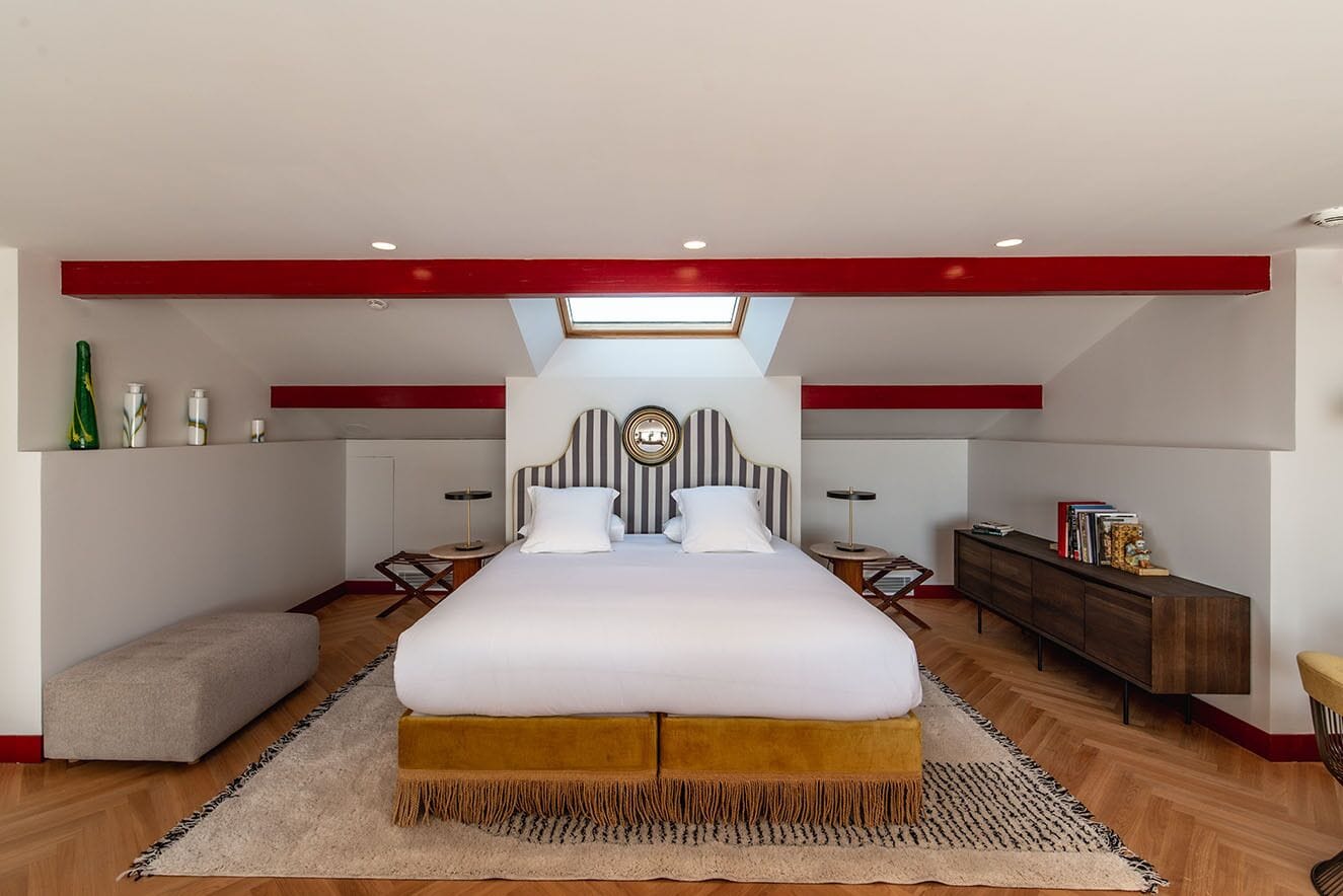 Une chambre à coucher moderne avec un grand lit, une lucarne, une table de chevet, un banc et un plancher en bois.