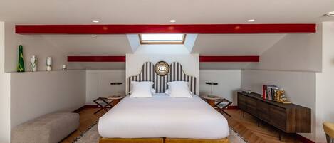 A modern bedroom with a large bed, a skylight, a bedside table, a bench, and a wooden floor.