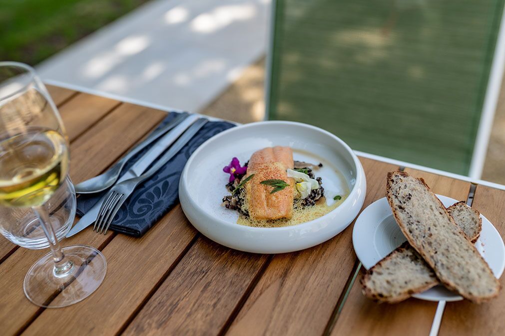 Une table en bois avec une assiette blanche remplie de nourriture, un verre de vin blanc et une serviette.
