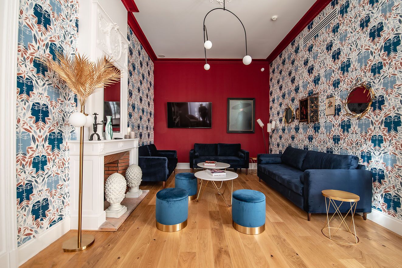A modern living room with a red accent wall, blue sofas, and a patterned wallpaper design.