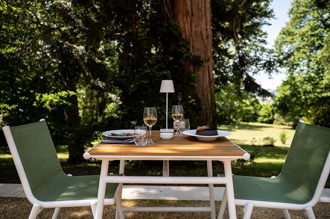 Een houten tafel met een lamp, twee stoelen en een bord eten, buiten geplaatst.