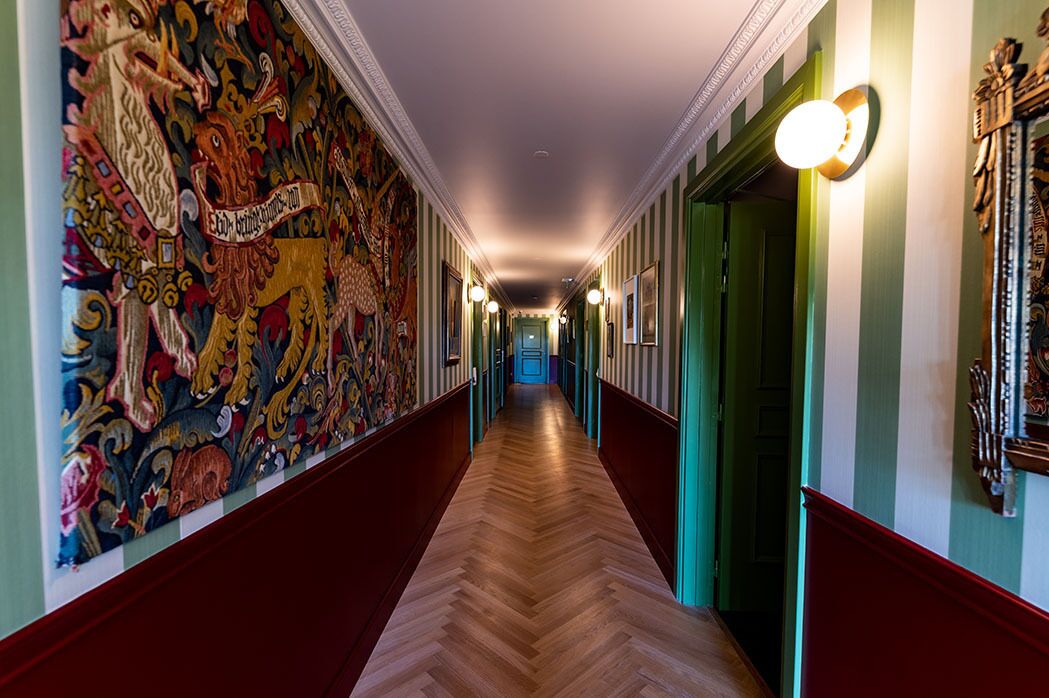 Käytävä, jossa on kalanruotokuviollinen lattia, raidalliset seinät ja värikäs seinämaalaus vasemmalla puolella.
