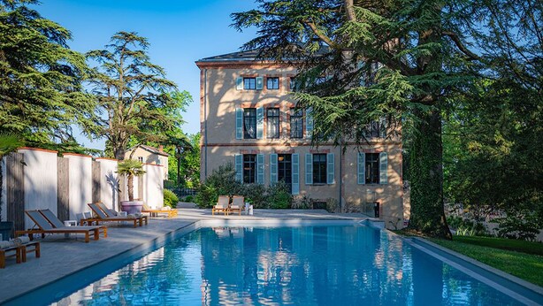 Uma piscina com espreguiçadeiras e um edifício grande com persianas.