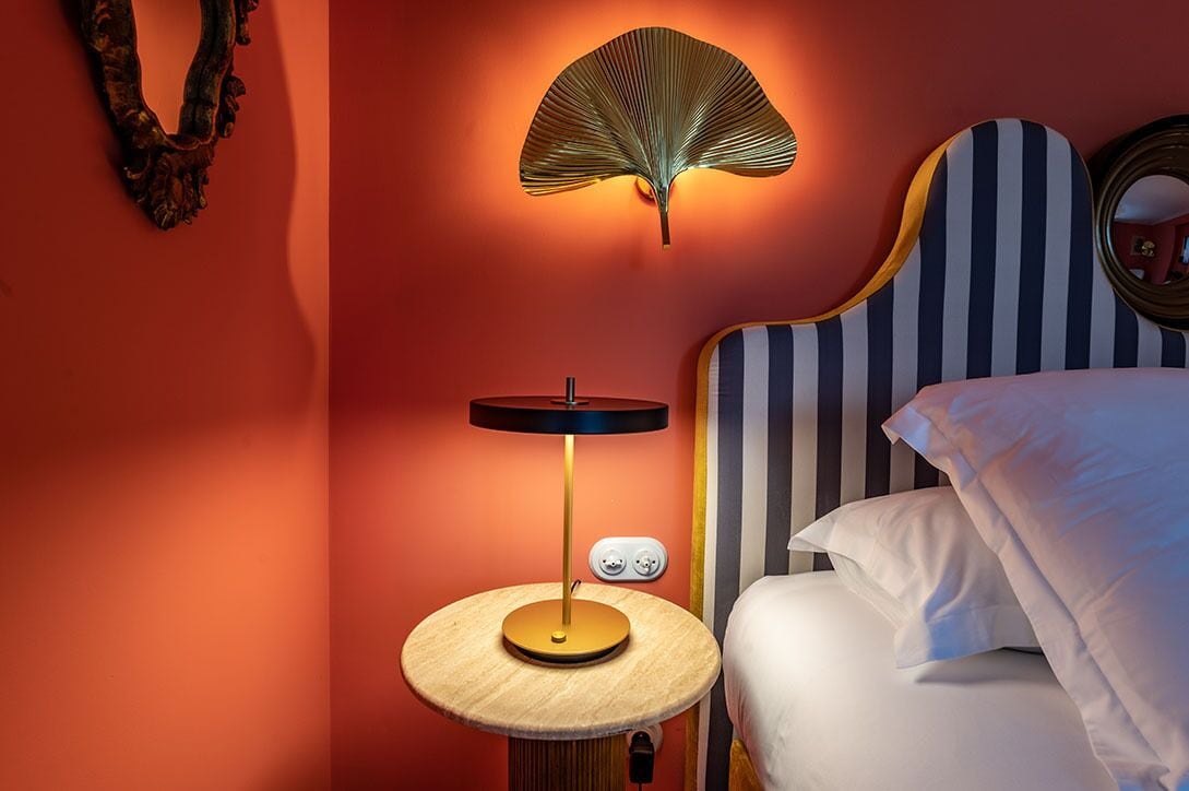 Un dormitorio con una cama, una lámpara de noche, una luz en la pared y un espejo.