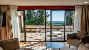 Uma sala de estar espaçosa com uma grande porta de vidro deslizante que dá para um terraço externo. O ambiente possui um sofá, uma mesa de centro e uma TV fixada na parede.