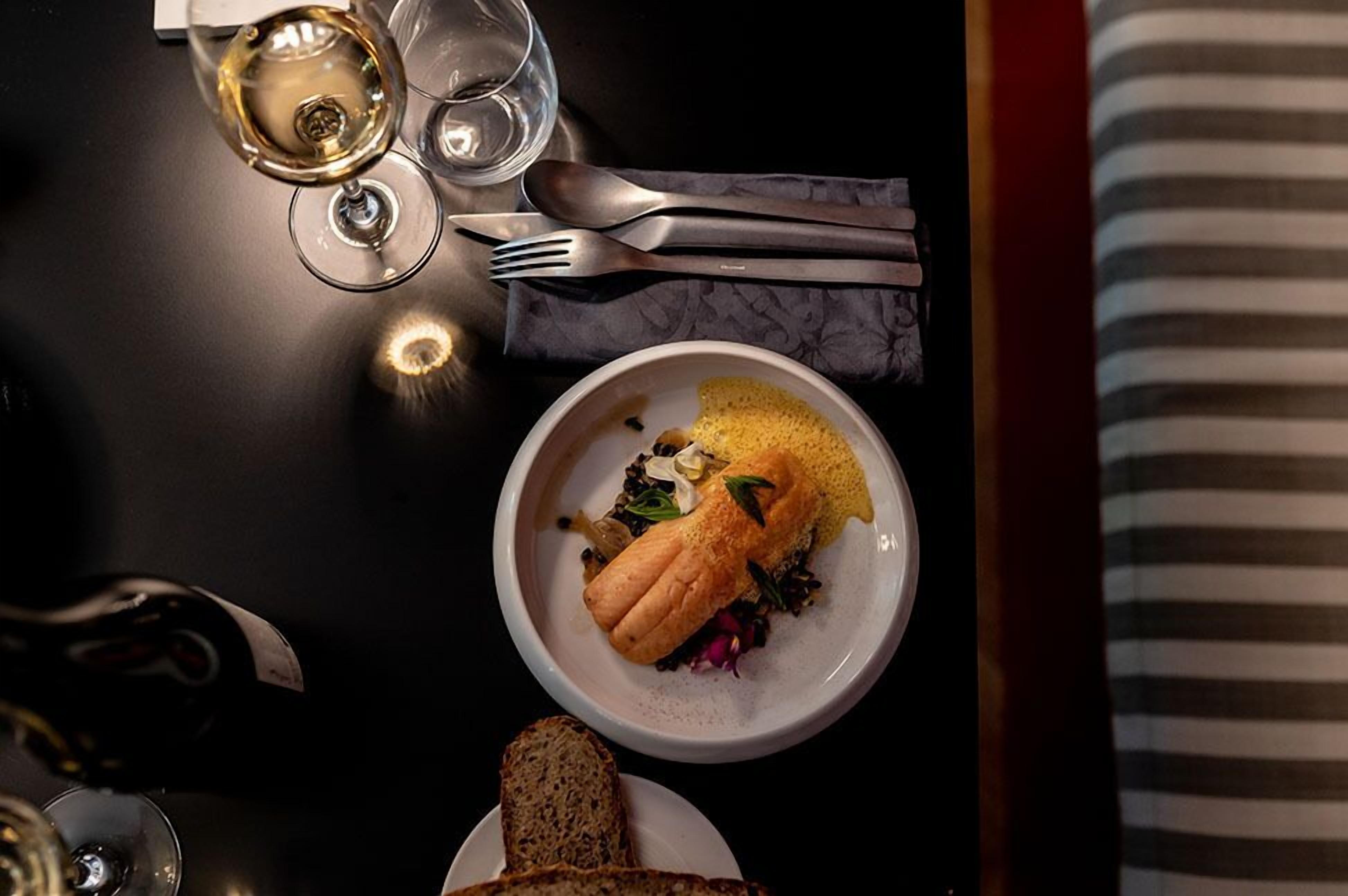 A dining table with a plate of food, a glass of white wine, and cutlery.