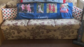 A sofa with a floral pattern, a blue cushion with family photos, and a vacuum cleaner.