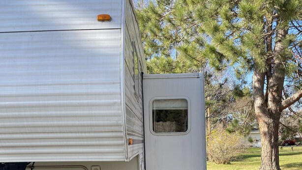 A white RV parked in a grassy area with a tree nearby.