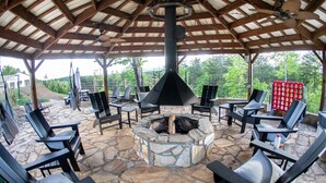 Un espacio al aire libre con techo, piso de piedra, sillas negras y una chimenea central.