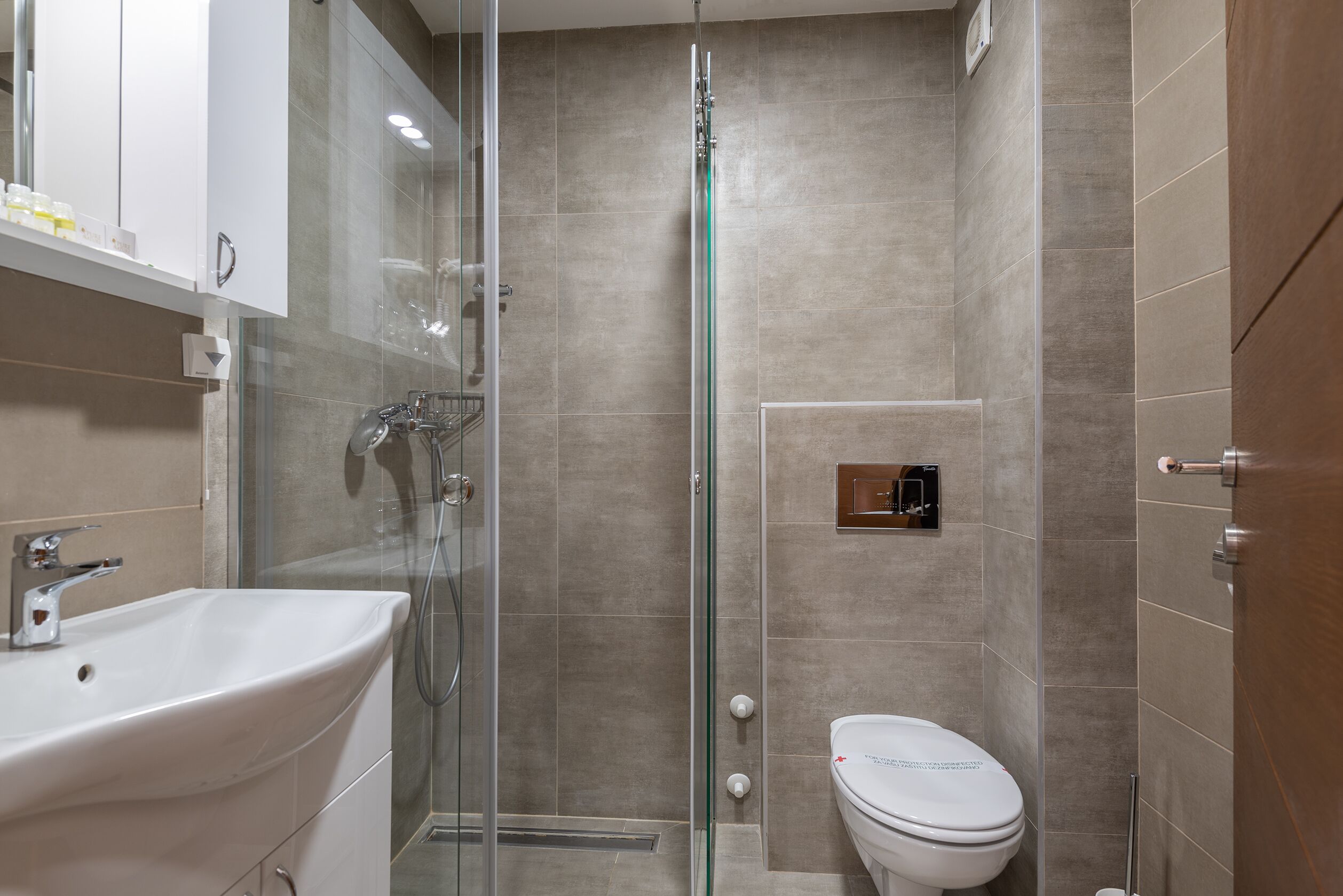 A modern bathroom with a glass-enclosed shower, a white sink, and a toilet.