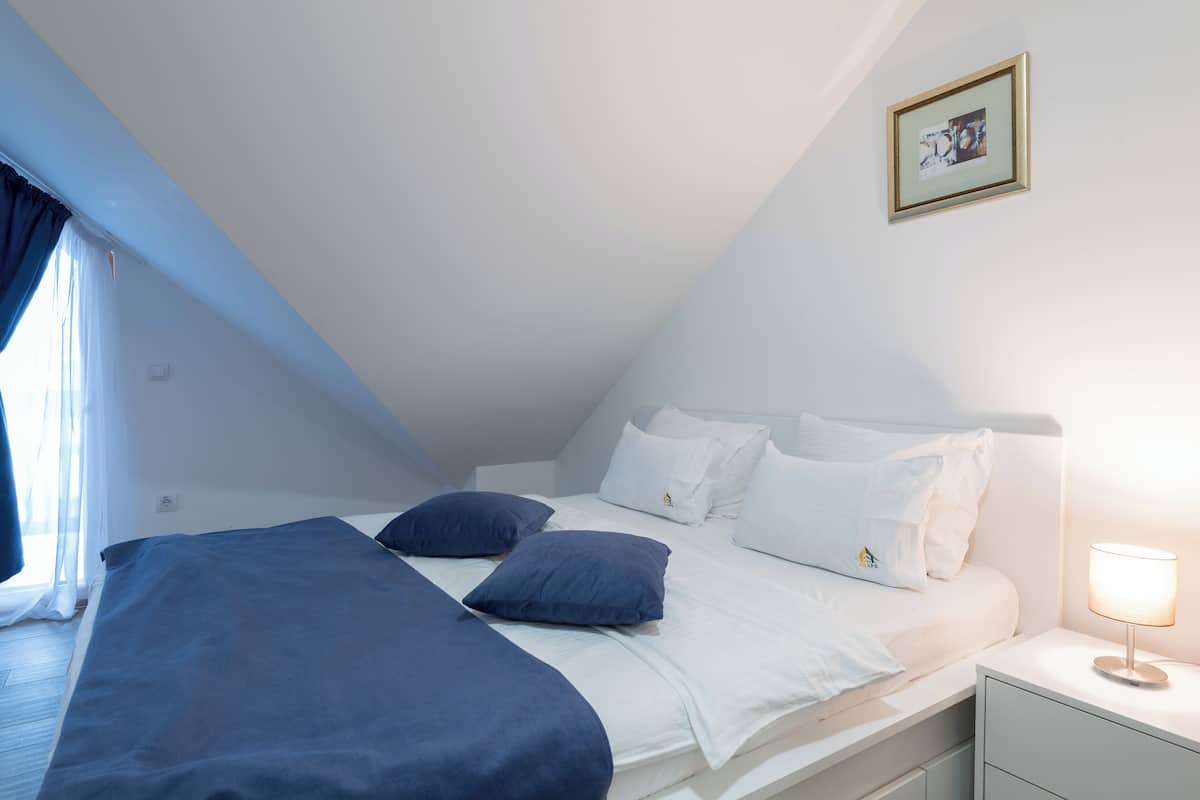 A bedroom with a bed, pillows, a bedside table with a lamp, and a framed picture on the wall.