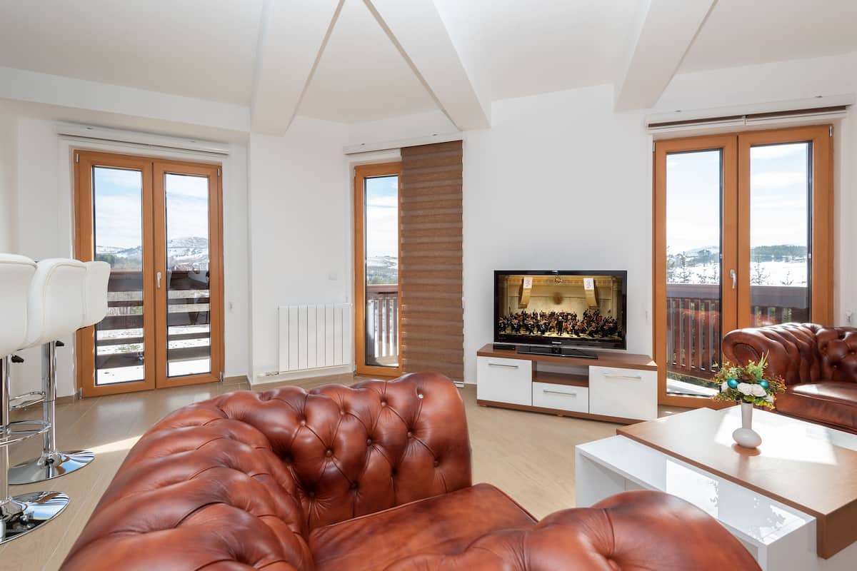 A modern living room with a leather sofa, a flat-screen TV, and a dining area.