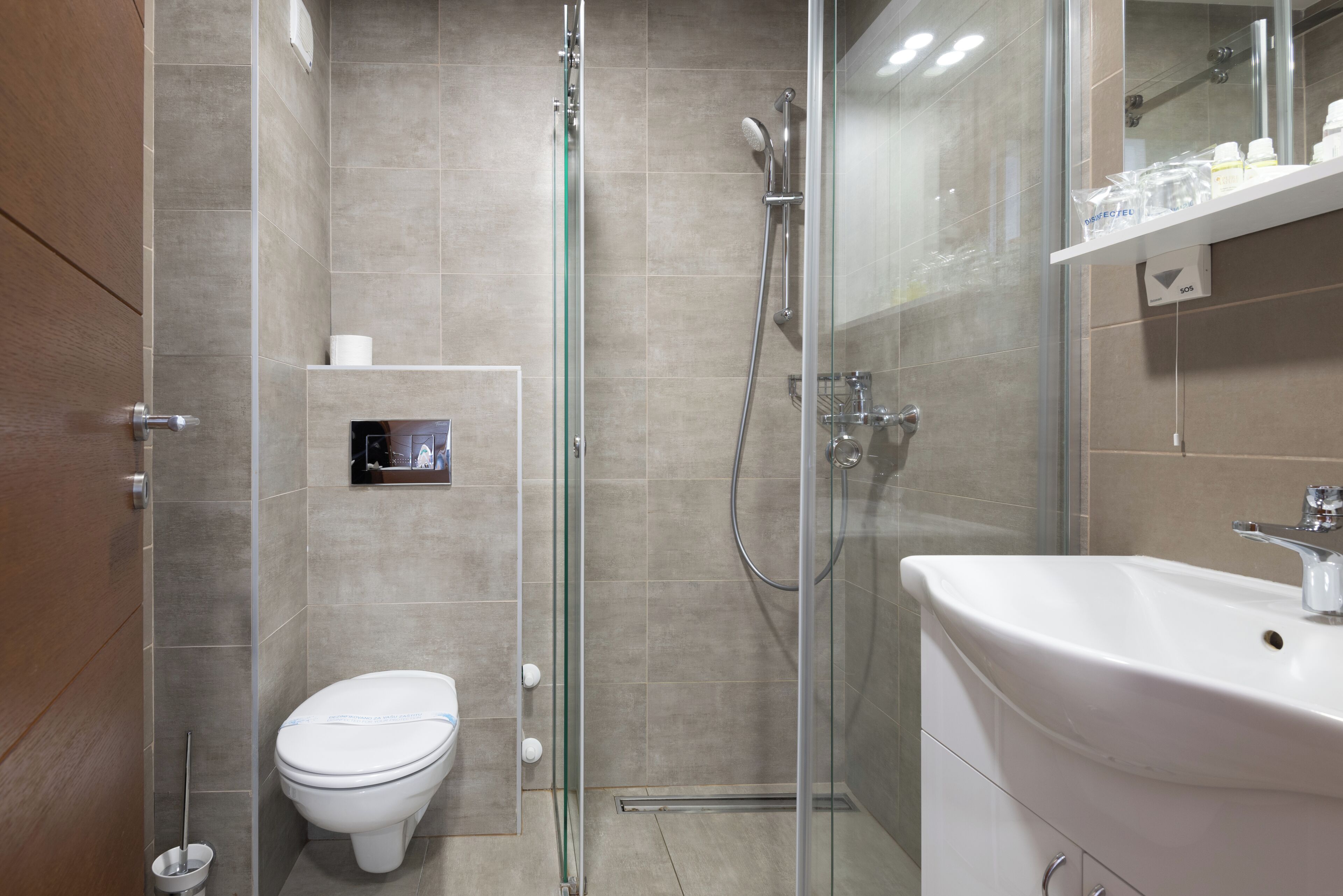 Un baño moderno con ducha envuelta en vidrio, un lavamanos blanco y un inodoro.