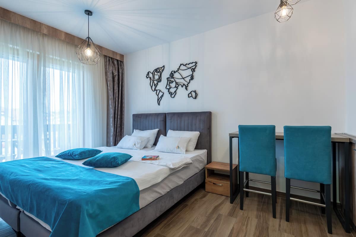 A modern hotel room with a large bed, two chairs, a desk, and a world map artwork on the wall.
