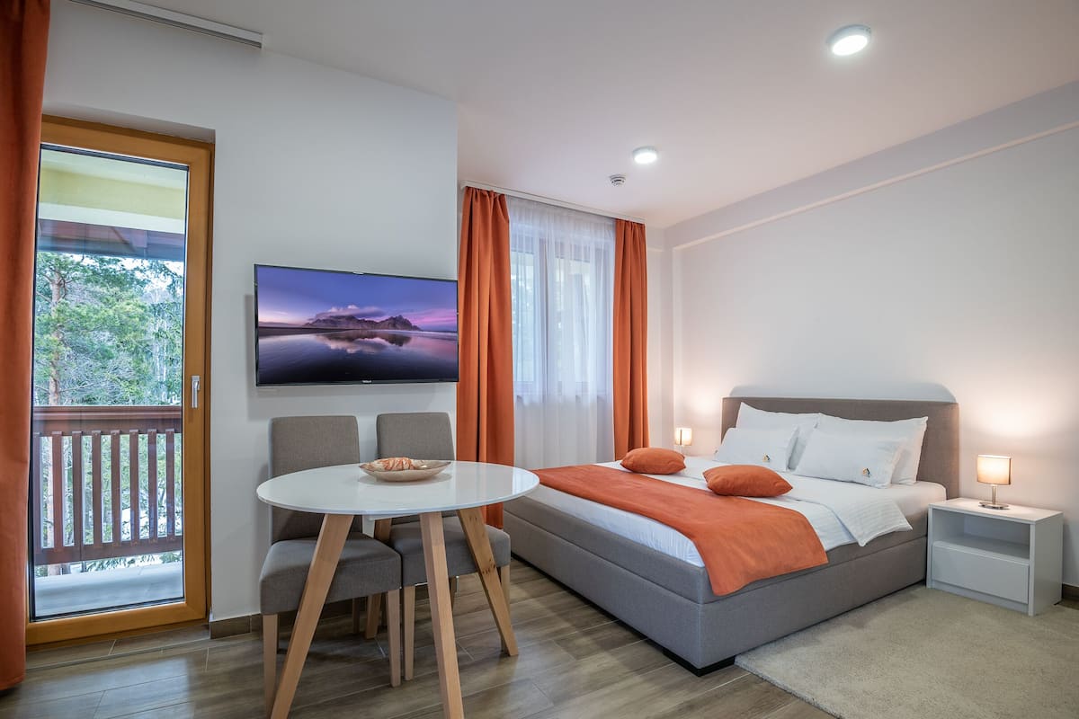 A modern bedroom with a bed, a TV, a small table, and a balcony.