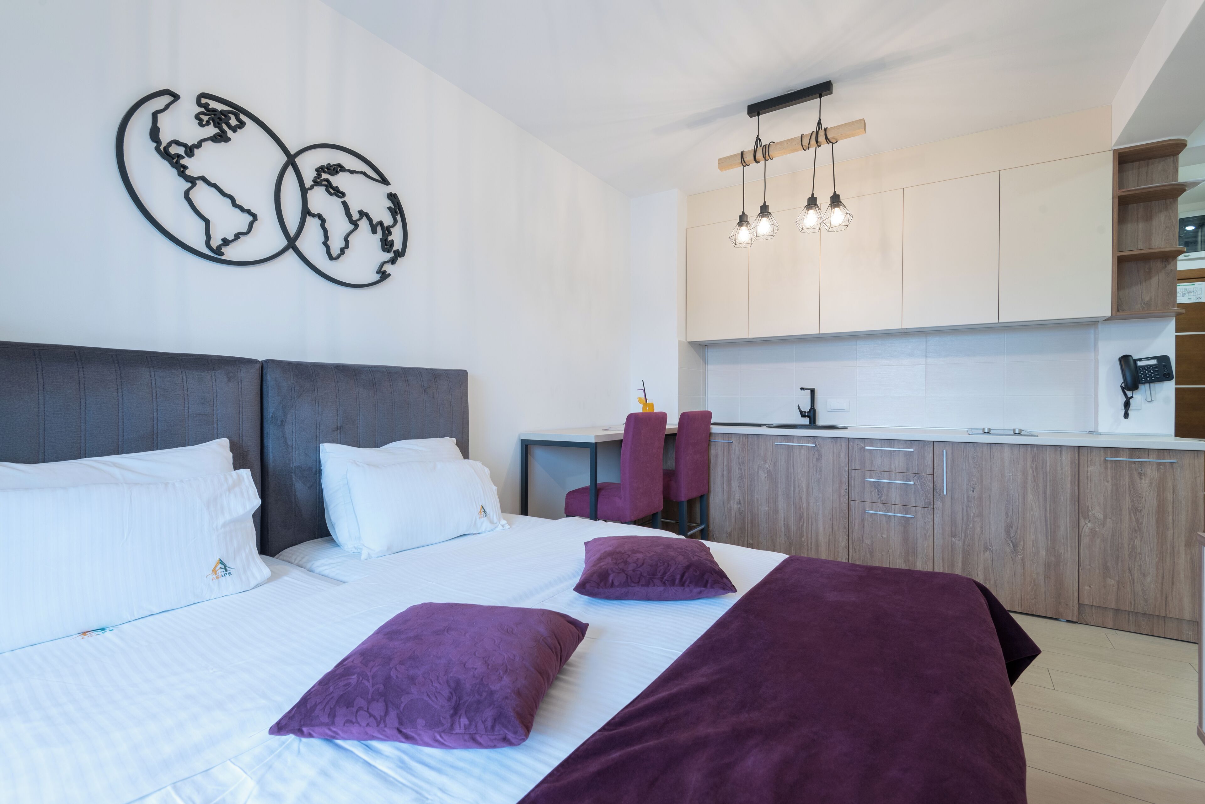 A modern hotel room with a large bed, a desk, and a kitchenette.