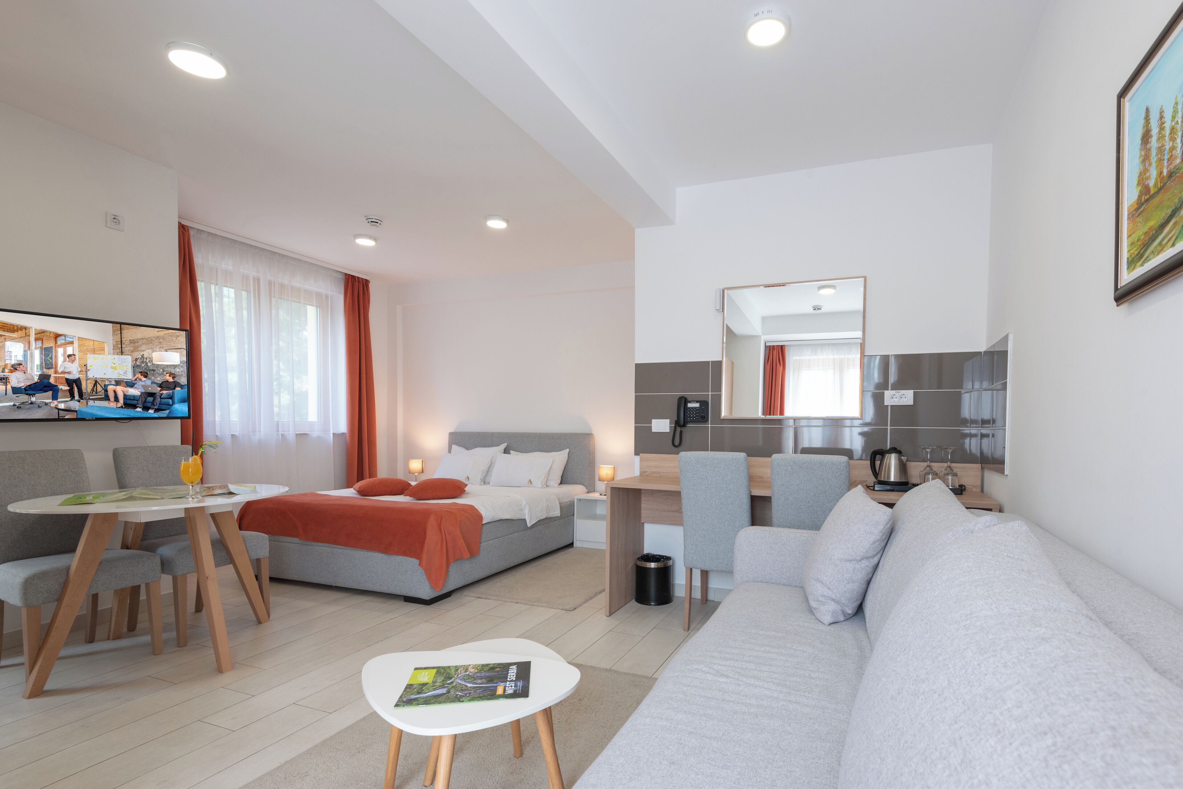 A modern hotel room with a bed, a sofa, a desk, and a dining area.
