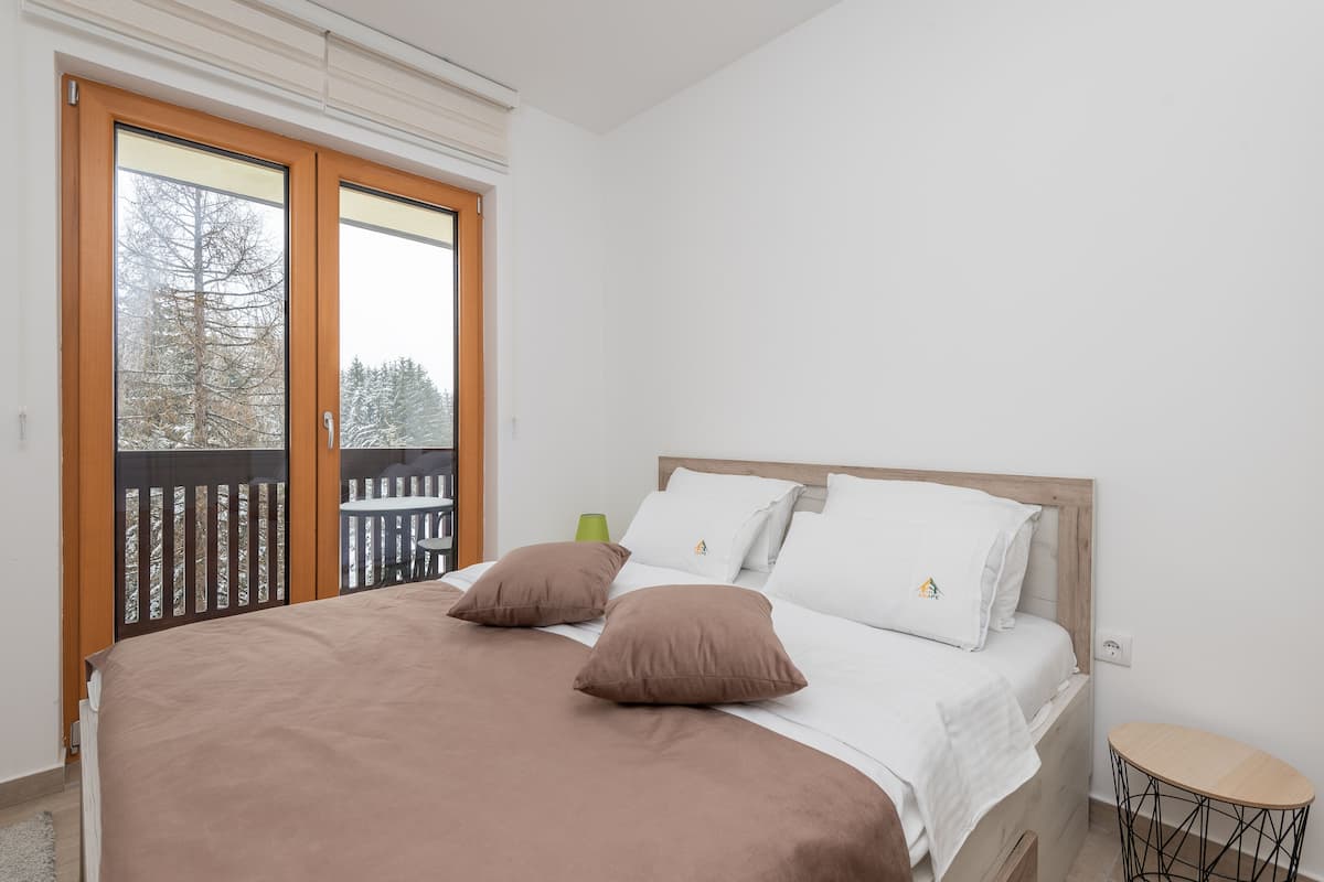 A bedroom with a bed, pillows, a bedside table, and a view of a balcony.