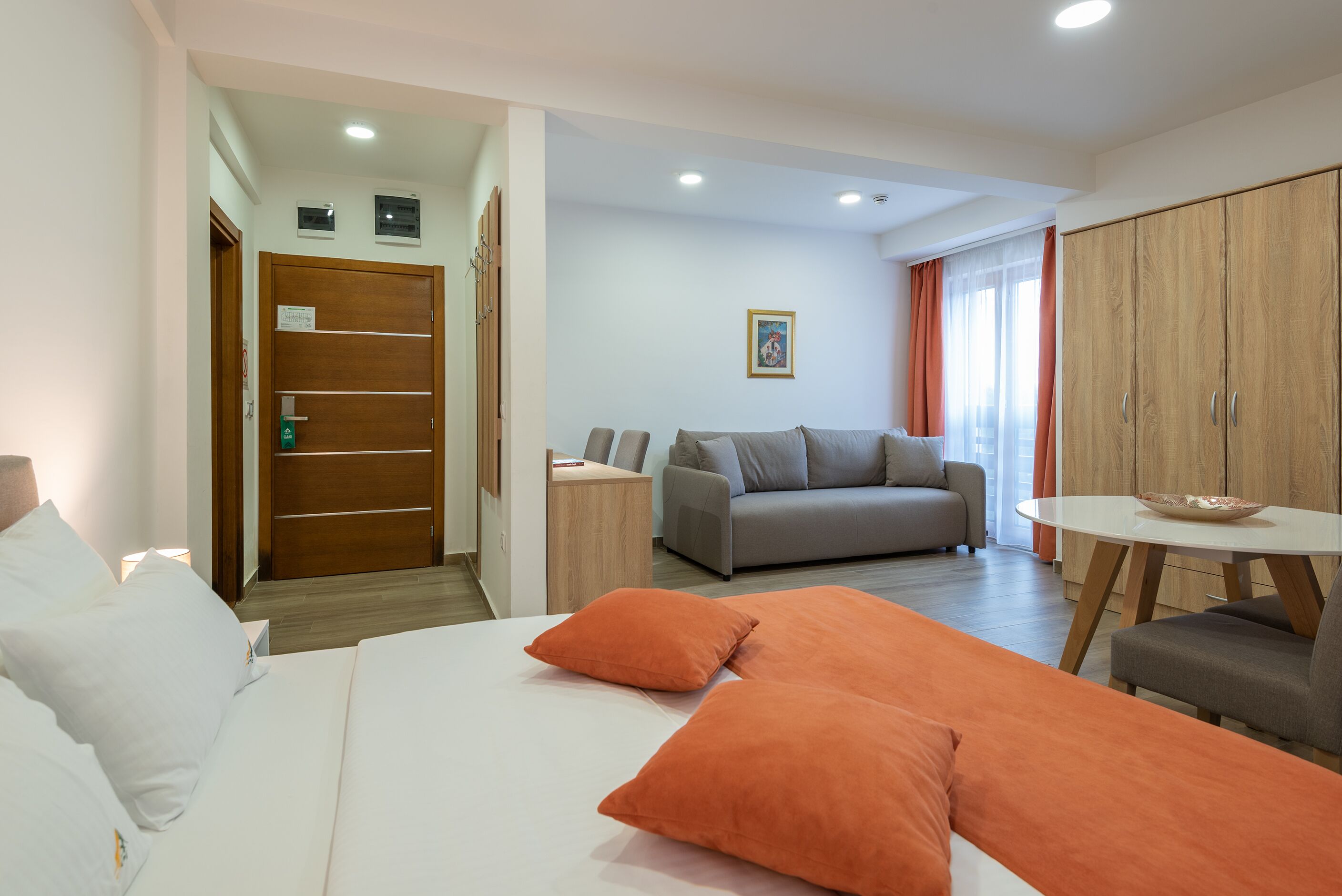 A hotel room with a bed, a sofa, a dining table, and a wardrobe.