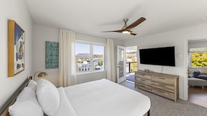 Un dormitorio con cama, cómoda, televisor y balcón con vistas.