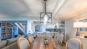A spacious dining area with a wooden table and chairs, a modern kitchen in the background, and a staircase leading to a loft.