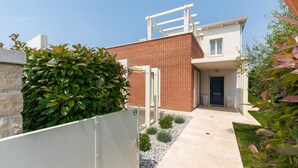 A modern house with a brick facade, a white door, and a small garden area with gravel and plants. - Elegant Villa Rafaelle with pool (Vabriga)