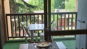Een eettafel gedekt met borden, bestek en glazen, met zicht op groen en een gebouw op de achtergrond.
