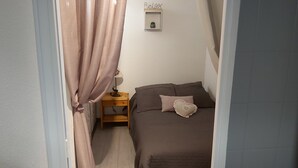 Een slaapkamer met een bed, nachtkastje, lamp en een plank met een plant.