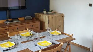 Een eetgedeelte met een houten tafel voor vier personen, een televisie aan de muur en een kast met een plant.