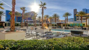 A rooftop pool area with lounge chairs, palm trees, and modern buildings in the background.