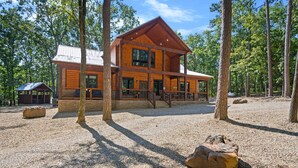 A wooden cabin with a large deck, surrounded by trees.